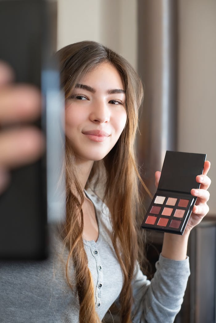 Asian woman holding a makeup palette during a vlogging session indoors.
